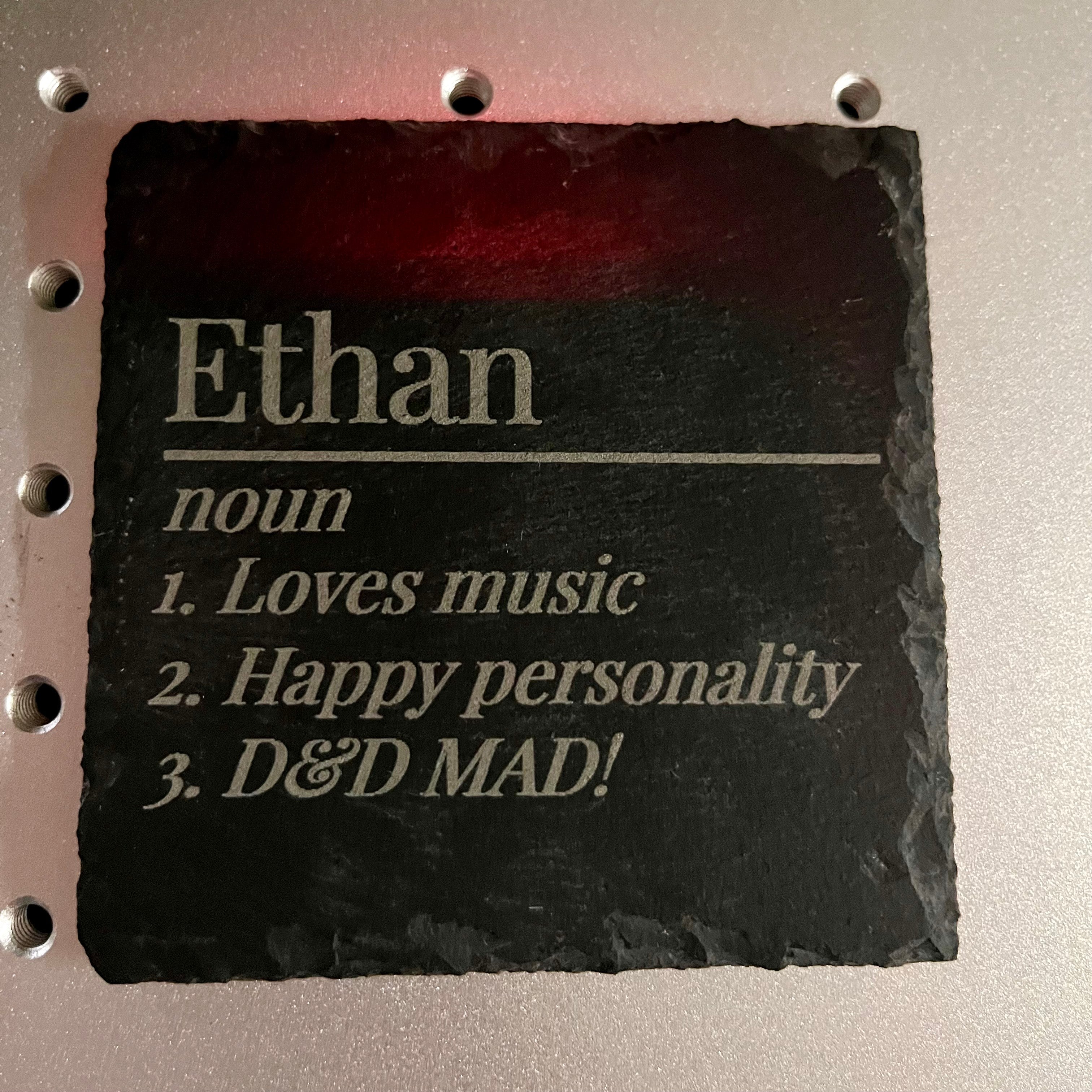 Square black slate coaster with rough edges featuring a dictionary-style definition for the name Ethan.